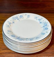 Stack of eight white bread and butter plates with blue floral pattern around edges, set on wooden surface