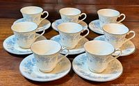 Eight paired tea cups and saucers arranged on wooden surface showing full set