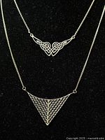Two vintage 925 sterling silver pendant necklaces displayed on a black velvet surface, clearly showing intricate filigree and web designs of the pendants.