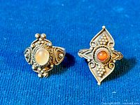 Two vintage Etruscan style sterling silver rings on blue fabric background, showing front view of moonstone ring on the left and carnelian ring on the right