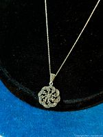 Pendant necklace displayed on black velvet stand showing the marcasite floral design pendant and small Figaro chain.