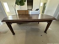 Full view of the antique large wooden table taken from a side angle, showing legs and top surface structure.
