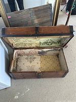 Open top view showing the interior of the wooden trunk lined with multi-patterned fabric, showing vintage wear.