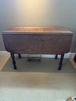 Front view of dark wooden table with drop-leaf sides folded down, turned legs visible.