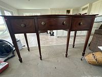 Front view showing the dark wood console table with three drawers having round metal handles and tapered legs
