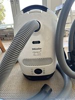 Front view of white Miele Olympus canister vacuum with attached grey hose