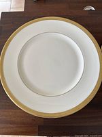 Close-up view of a large white plate with a detailed gold trim around the edge showing classic Royal Doulton design.