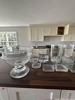 Photo of clear glass flower pots and vases in multiple shapes on a wooden surface indoors.