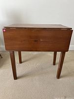 Front view of the brown wooden drop leaf table with both leaves down.