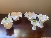 Five white hobnail milk glass items on dark surface: 3 vases with wavy ruffled rims and 2 candleholders with wavy edges