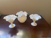 Front view of three Fenton milk glass pieces: two hobnail goblet dishes with wavy rims and one round hobnail vase with ruffled top.