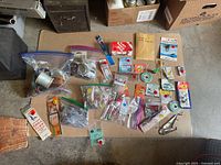 Photo showing wide assortment of fishing accessories laid out on cardboard including spools of fishing wire, various packages of hooks, metal bait, and small packets.