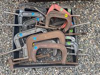 Photo showing a pile of approximately 14 vintage steel C-clamps in various sizes and finishes on gravel background.