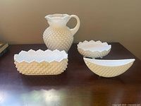 Pitcher and 3 bowls arranged on wooden surface, showing hobnail texture and scalloped edges.