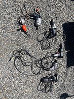 Six vintage electric hand drills laid out on gravel surface, all with attached cords and varying colors and styles.