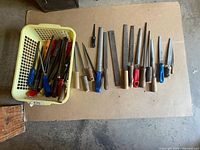 Bin of various vintage metal files with different handle types and colors, laid out on cardboard