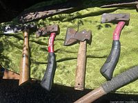 Four vintage axes laid side by side on green patterned fabric outdoors, showing handles and metal axe heads with wear, rust, and paint chipping.