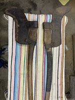 Photo of two vintage brush axes with wooden handles and curved steel blades, each covered with a leather sheath, laid out on a knitted mat.