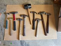 Top view photo of nine assorted vintage hammers laid out on corrugated cardboard on a concrete floor.