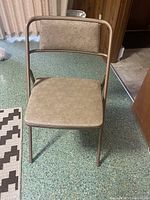 Front view of one vintage mid-century modern folding chair showing metal frame and vinyl seat and backrest upholstery.
