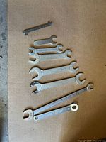Seven vintage wrenches arranged on a surface, showing clear size markings and engravings. Two combination wrenches include boxed end sides, others are open end only.