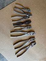 Seven vintage metal pliers laid out on cardboard, showing variety of types and sizes.