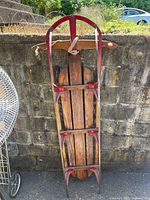 Full view of the vintage Royal Racer sled leaning against a stone wall outdoors.