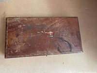 Closed wooden box with worn finish and faded logo or marking on the lid.