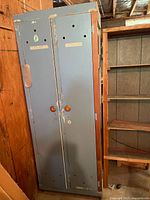 Full view of vintage two-door wooden locker/storage cabinet in worn blue-gray paint with labels on doors