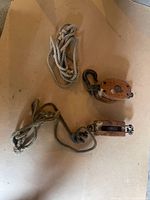 Two vintage wooden pulleys each with attached ropes on a flat surface. One pulley has double wheels while the other has single wheel, hooks with patina visible.