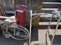 Wheelchair and walker positioned side by side outdoors, showing red fabric seat and back on wheelchair and metal frame walker