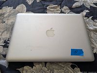 Closed view of the Apple laptop from top showing silver aluminum body with Apple logo and a blue sticker marked '13"'