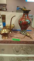 View of brass pitcher, enameled vase, and brass container on a counter with other household items in the background.
