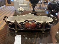 Front view of decorative porcelain and brass footed centerpiece with handles, showing black porcelain with red central medallion and floral garlands in porcelain relief on sides, resting on brass feet.