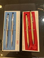 Two Cross pen and pencil sets in original boxes, one silver tone on blue lining, one gold tone on red lining.
