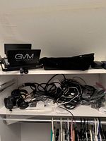 GVM branded LED light and assorted tangled cables and electronic items on shelving.