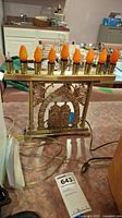Full view of the gold-tone metal electric menorah with nine flame bulbs, one bulb broken, showing the complete structure including power cord.