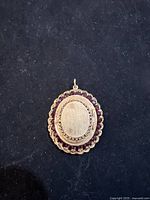 Closed front view of oval gold locket on black background, showing plain center and garnet border.
