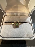 Ring in a grey velvet display box showing the flower design with a small green center stone.