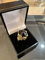 Ring displayed in a black jewelry box showing the faceted oval stone and textured gold shank.
