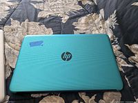 Closed view of turquoise HP laptop lid with HP logo and a small piece of blue tape labeled 75