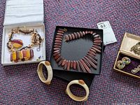 Overall view of wooden look necklace and bracelet set, cream-colored bangles, polished stone bracelet, and box with brooches and earrings