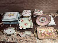 Seven pieces of Limoges porcelain trinket dishes and boxes displayed on marble surface, showing variety of shapes and colors with floral and gilt decoration.