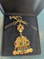 Gold tone necklace with an ornate pendant featuring red and green stones and small dangling gold coin charms.