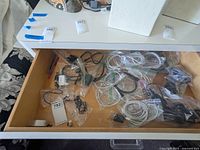Top view of drawer showing mixed power cords, earbuds, and chargers loosely packed in plastic bags