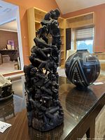 Full view of hand-carved African tribal sculpture placed on a table with other decorative items in the background.