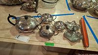 Full view of silverplate tea set including teapot, sugar bowl, creamer, and leaf dishes, plus the orange ceramic boat.