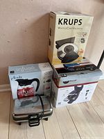 Photo showing all the boxed appliances together including Primula Infuse pitcher, Krups waffle maker box, Itantonio waffle maker, and Keurig coffee maker box.