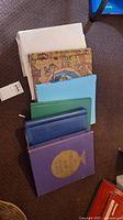 Six assorted stamp albums laid out on carpet, showing different binder colors and one with vintage map design cover.