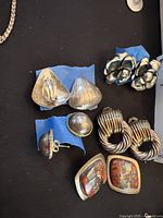 Top-down view of five pairs of sterling silver earrings including clip-on and pierced styles laid out on a dark surface.